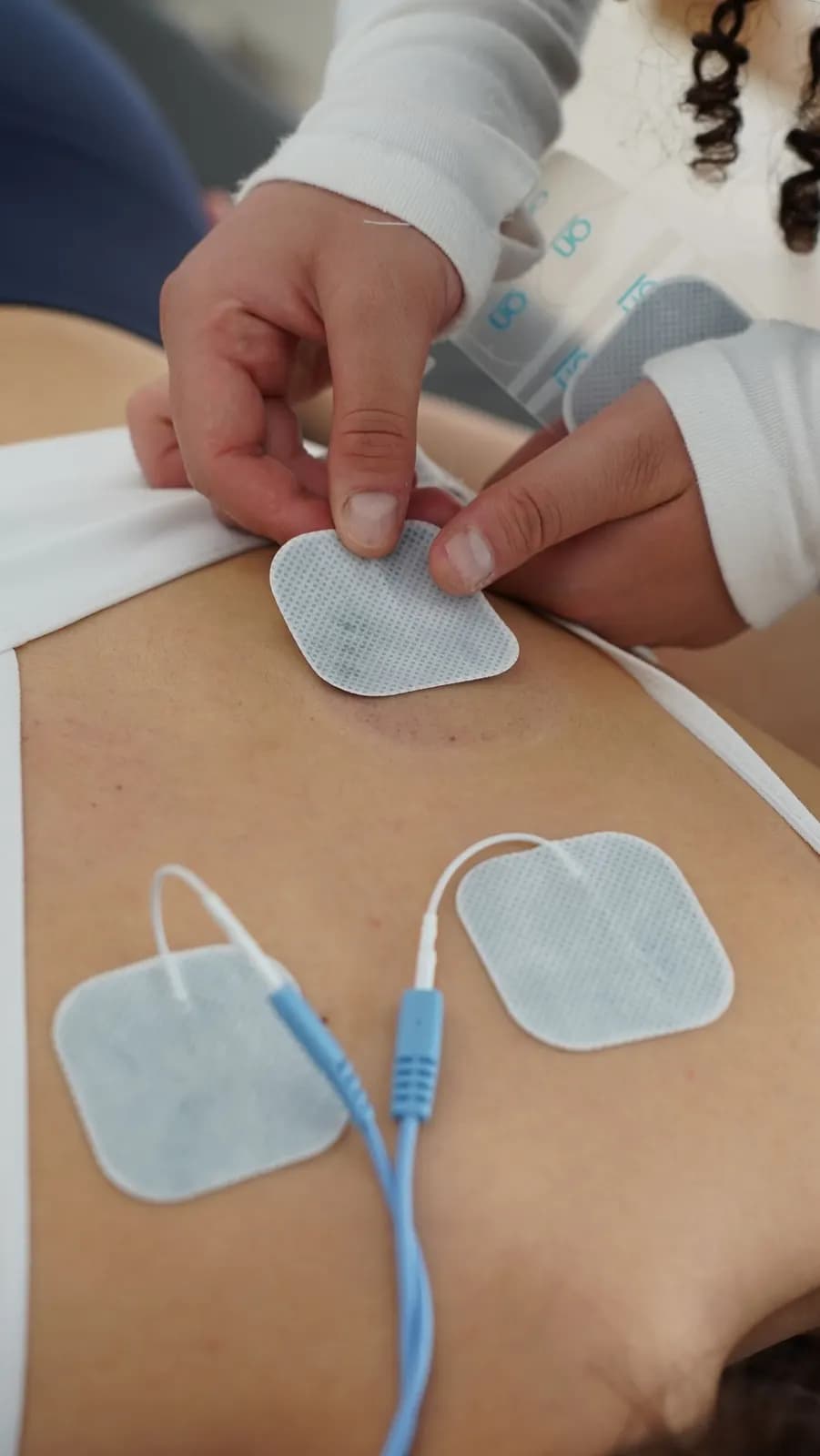 Fizyoterapist, hastanın beline elektrot pedlerini yerleştiriyor